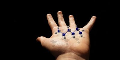 Child's hand holding a molecular structure model with blue and gray atoms, set against a dark background.
