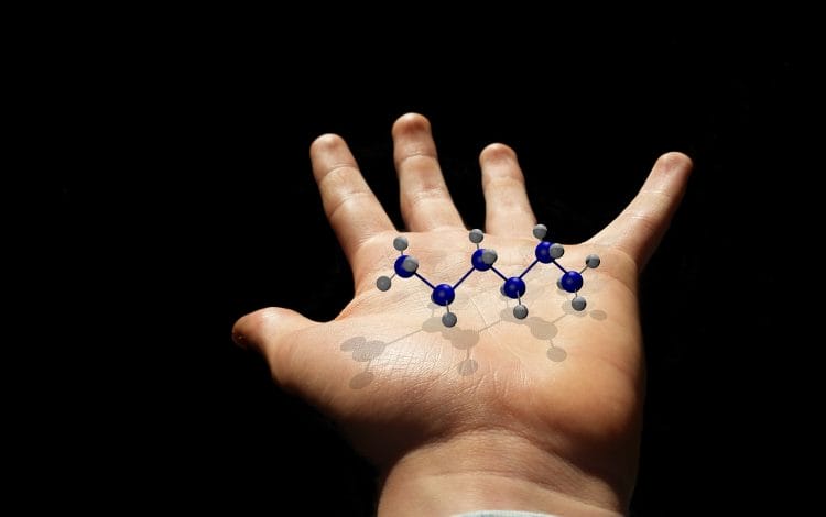Child's hand holding a molecular structure model with blue and gray atoms, set against a dark background.