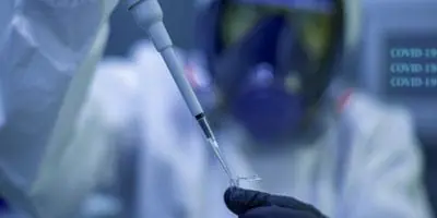 Scientist wearing full protective gear and mask, using a pipette to transfer a liquid sample in a laboratory setting