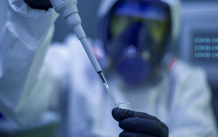 Scientist wearing full protective gear and mask, using a pipette to transfer a liquid sample in a laboratory setting