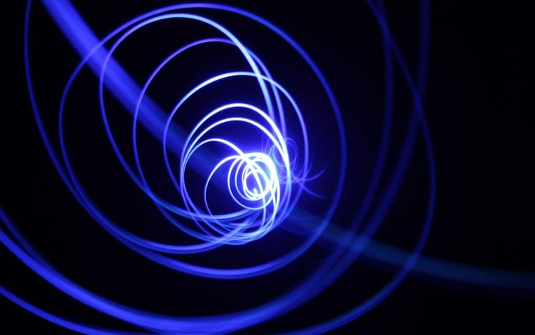 Abstract image of a spiral pattern made of blue light trails against a dark background.