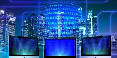 Futuristic digital illustration showing three computer monitors displaying binary code
