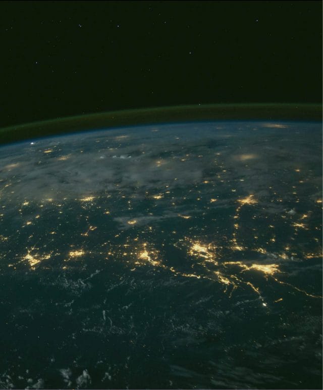 Night view of Earth from space, with city lights illuminating the surface.