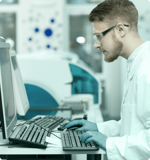 Scientist at a desktop computer wearing a lab coat, glasses and protective gloves