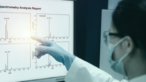 Scientist pointing at a spectrometry analysis report on a computer screen in a laboratory.