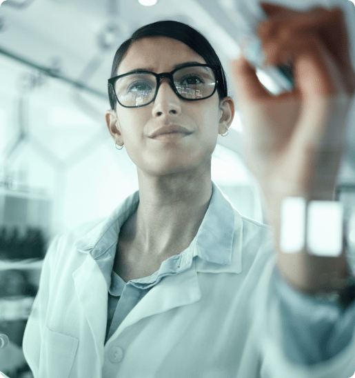 Female life scientist in a lab coat and glasses, examining a sample in a research facility.