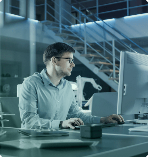 Scientist working on a computer in a modern office with industrial equipment in the background.