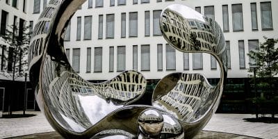 Reflective abstract sculpture in front of a modern building with numerous windows.
