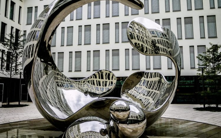 Reflective abstract sculpture in front of a modern building with numerous windows.